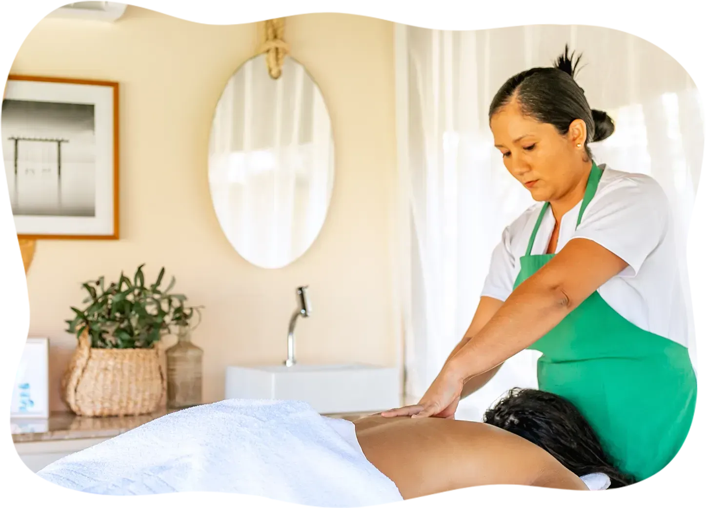 Uma mulher com um avental verde está fazendo uma massagem em uma mulher deitada na cama.