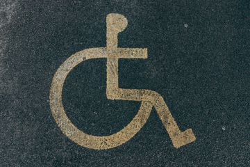 A white, stenciled International Symbol of Access (wheelchair symbol) painted on dark asphalt.