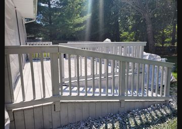 A white wooden deck ramp with railing slopes down towards a backyard covered in gravel and lawn.