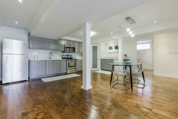 A modern, open-concept kitchen with grey cabinets, stainless steel appliances, and a small dining table on wood floors.