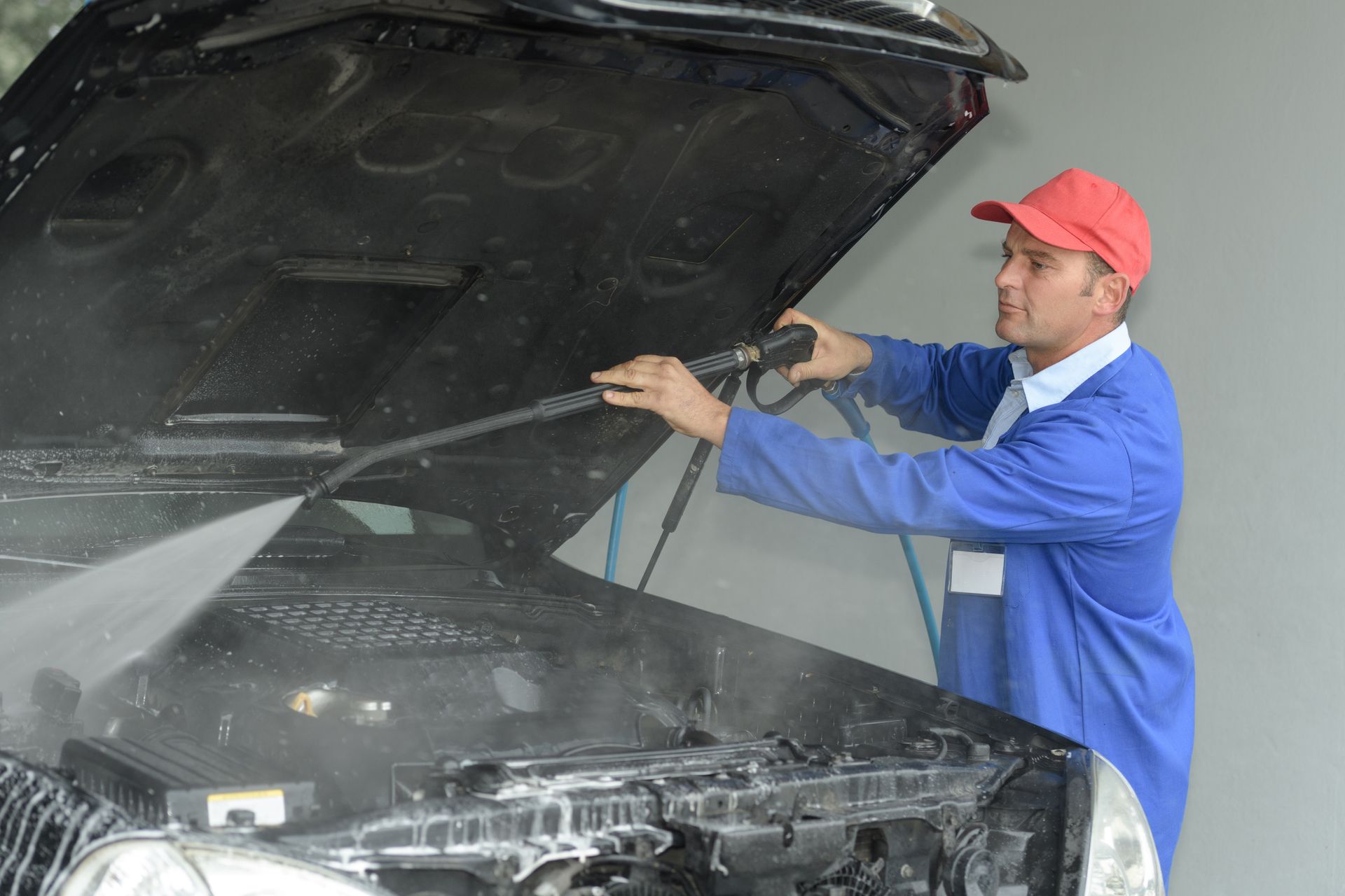A man in a red hat is cleaning the hood of a car