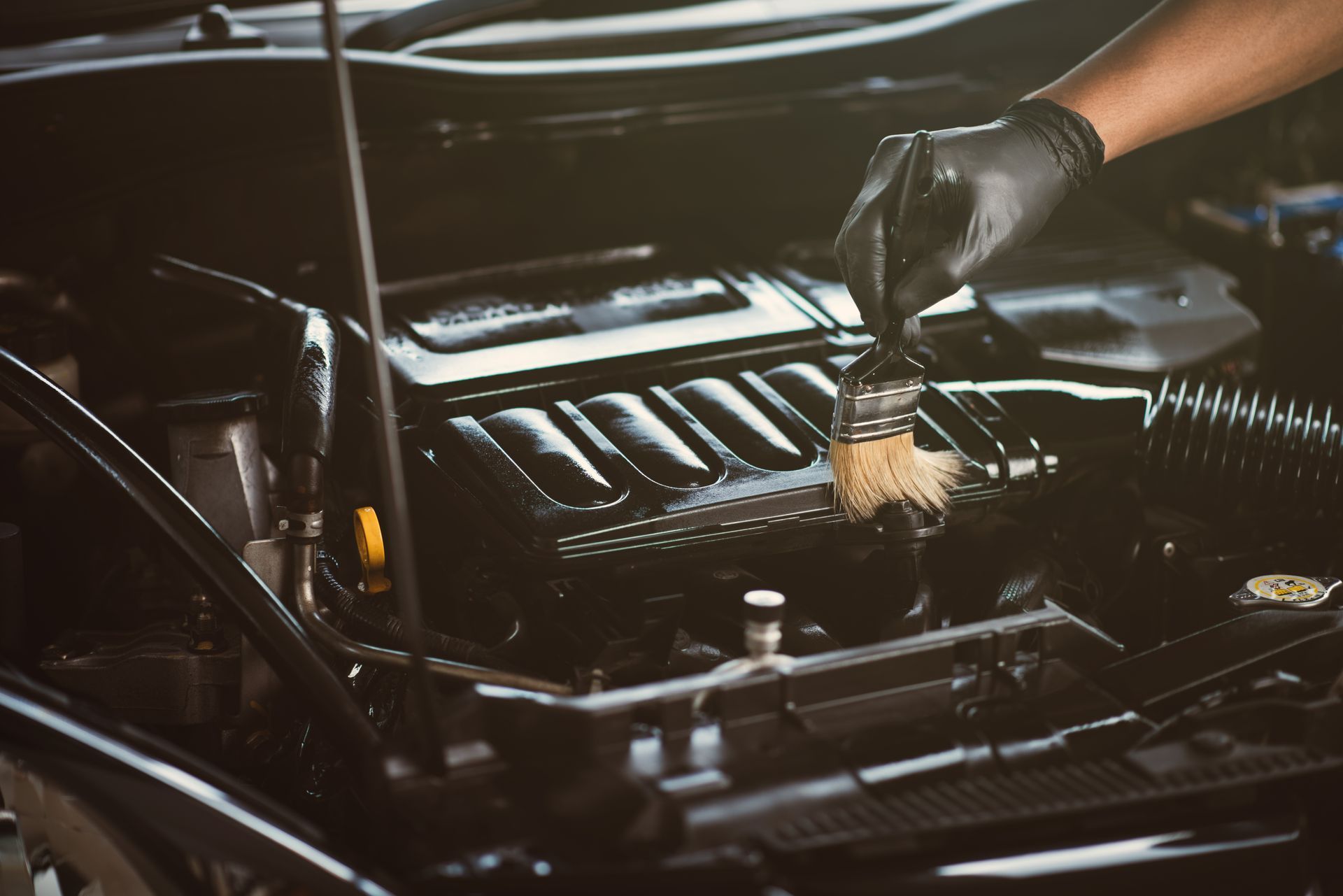 A person is cleaning the engine of a car with a brush.