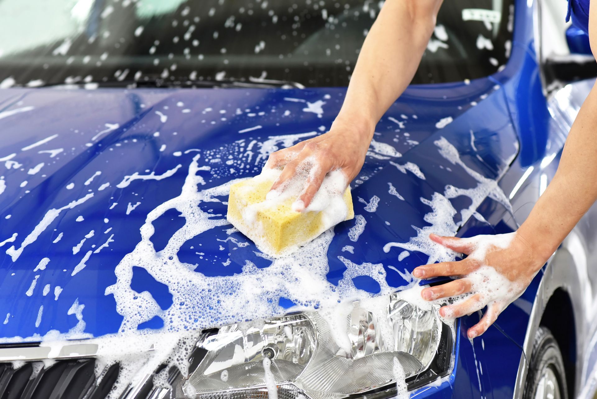 A person is washing a blue car with a sponge.