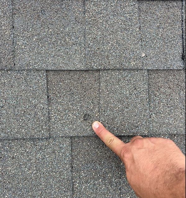 A person is pointing at a hole in a roof shingle.