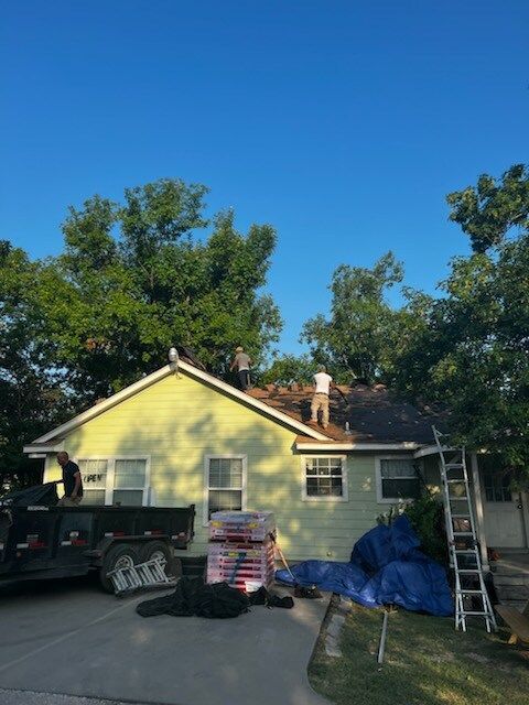 Two men are working on the roof of a yellow house.