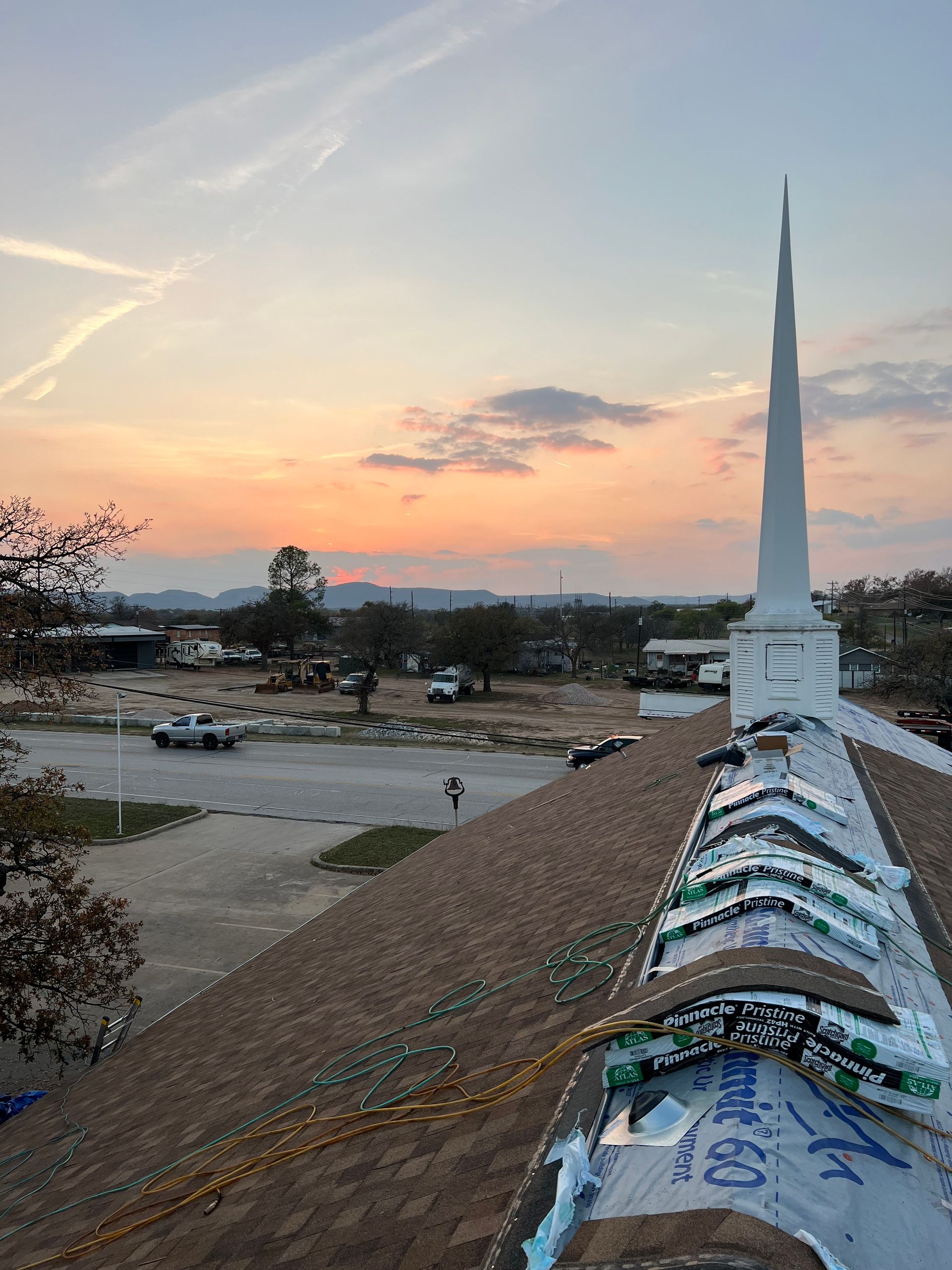A roof with a steeple on top of it and a sunset in the background.