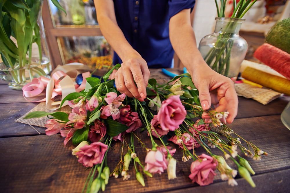 A Woman is Arranging Flowers on a Wooden Table — The Flower Station Townsville In Kirwan, QLD