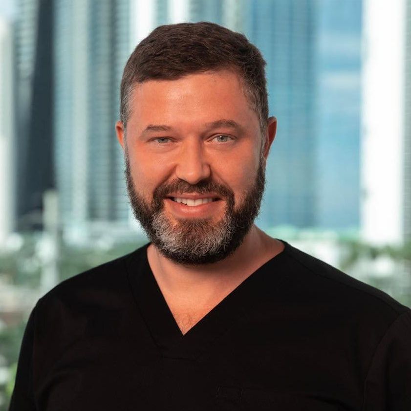 A man with a beard is wearing a black shirt and smiling for the camera.