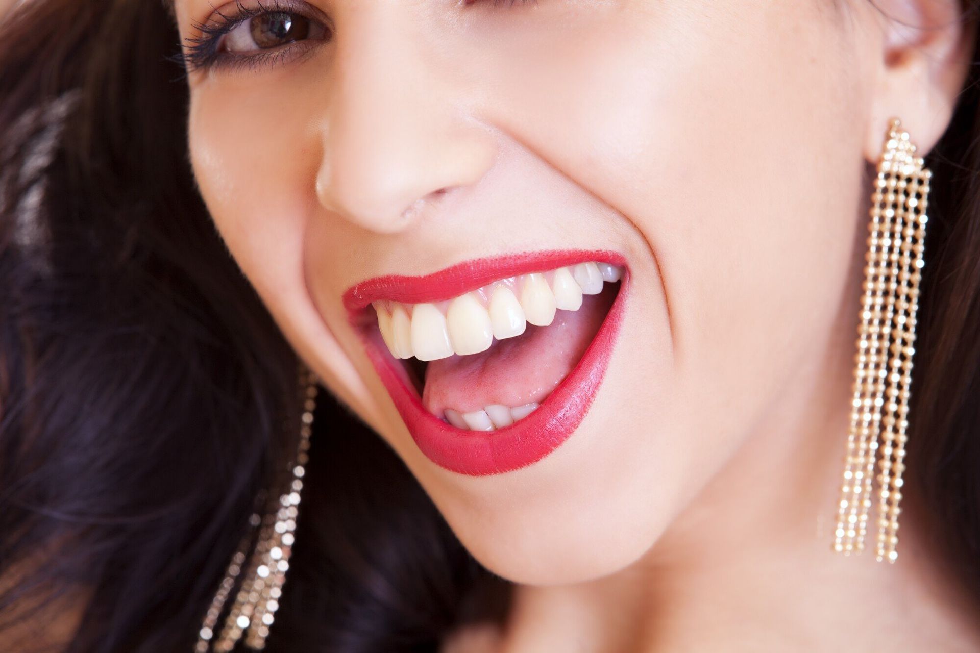 a woman wearing red lipstick and gold earrings is smiling .