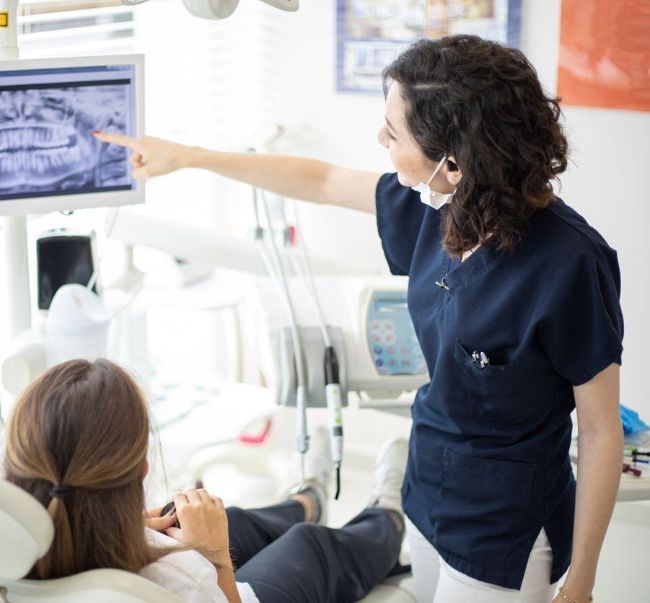 A female dentist is pointing at an x-ray of a patient 's teeth