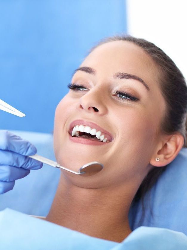 A woman is smiling while having her teeth examined by a dentist.