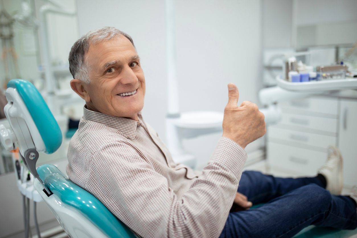 A man is sitting in a dental chair and giving a thumbs up.