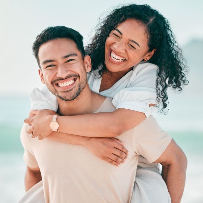 A man is carrying a woman on his back on the beach.