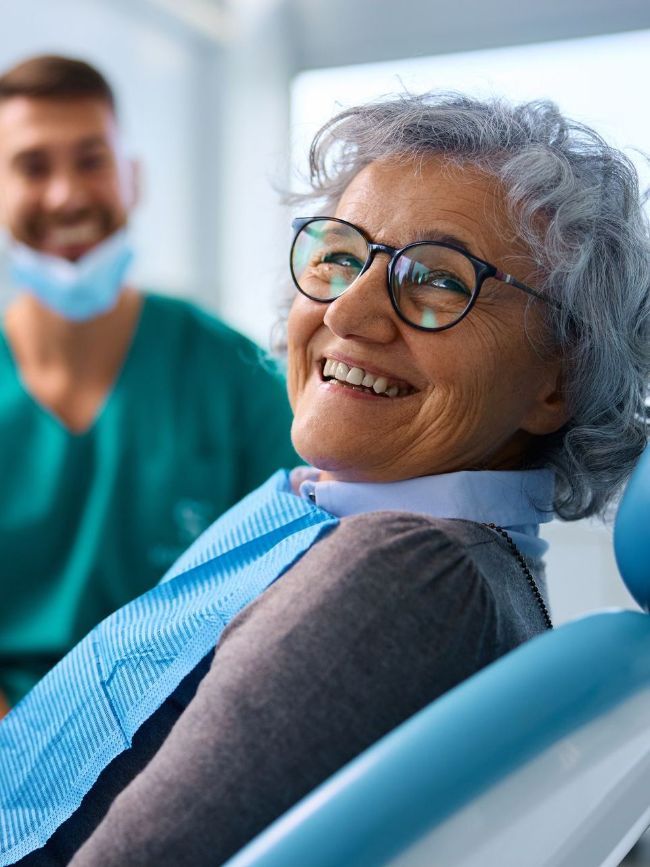 An elderly woman is smiling while sitting in a dental chair.