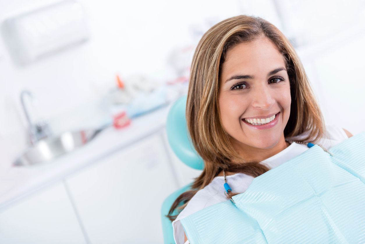 A woman is smiling while sitting in a dental chair.