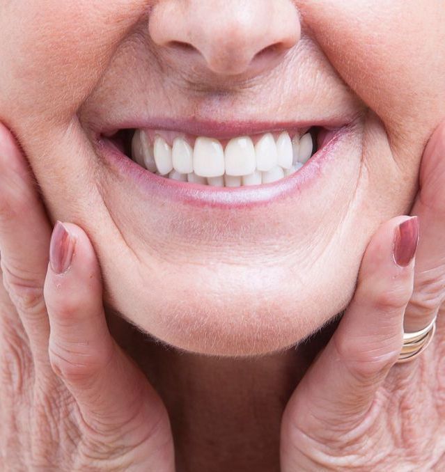 An elderly woman is smiling with her dentures