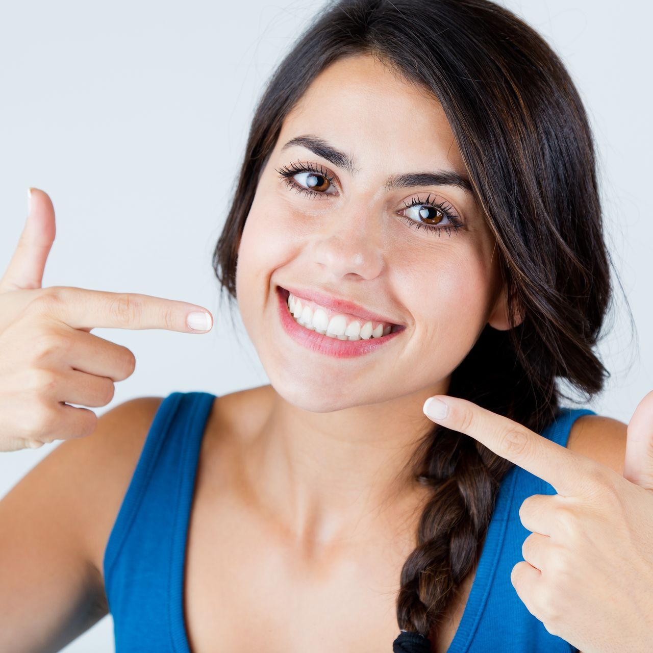 A woman in a blue tank top is smiling and pointing at her smile