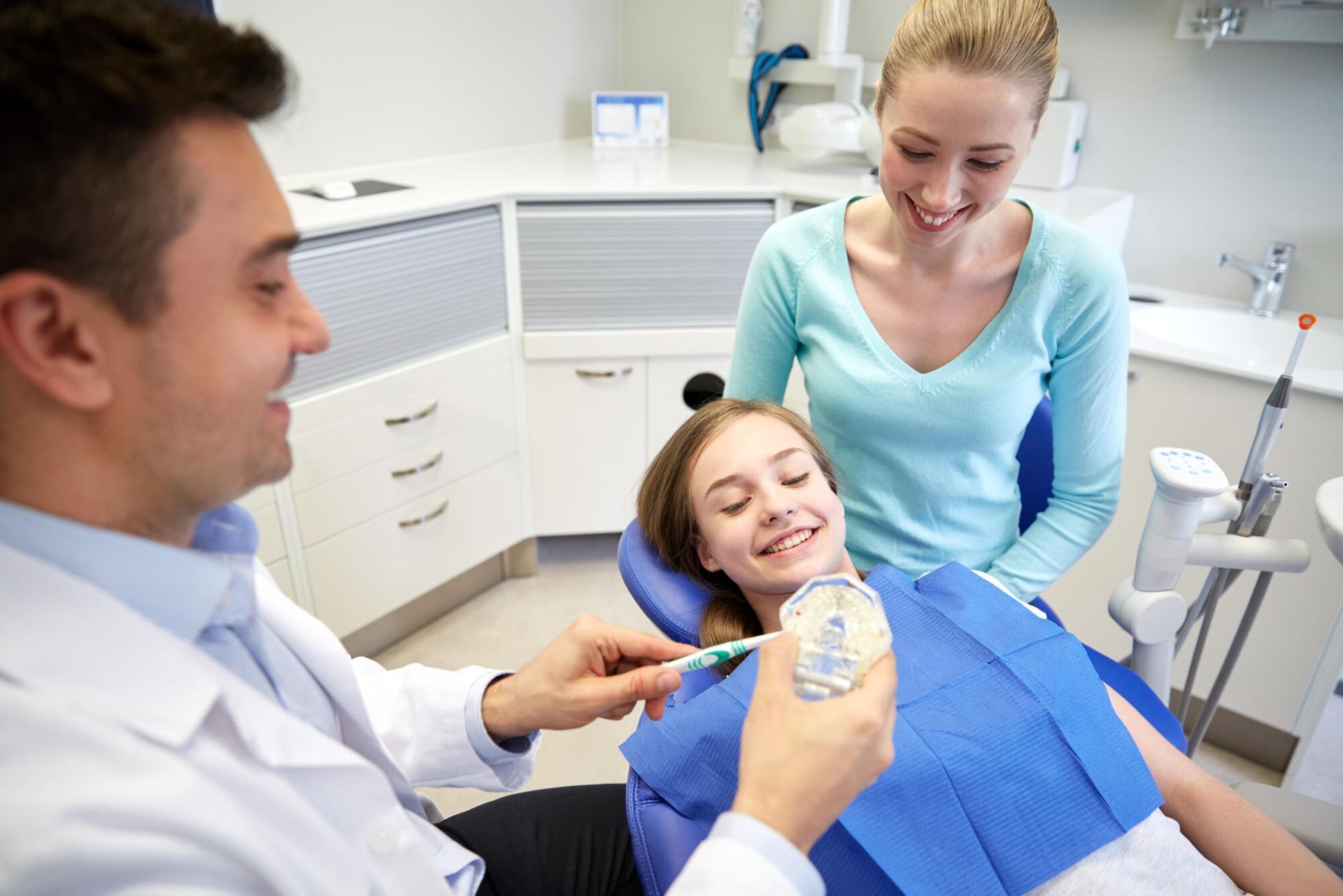 A young girl is sitting in a dental chair while a dentist examines her teeth.