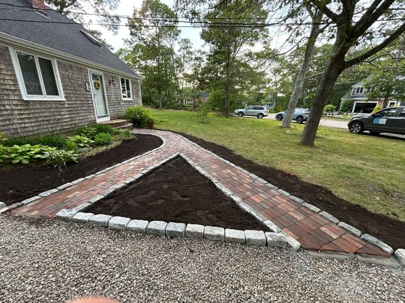 A grassy yard borders a row of bushes and trees under a clear blue sky.