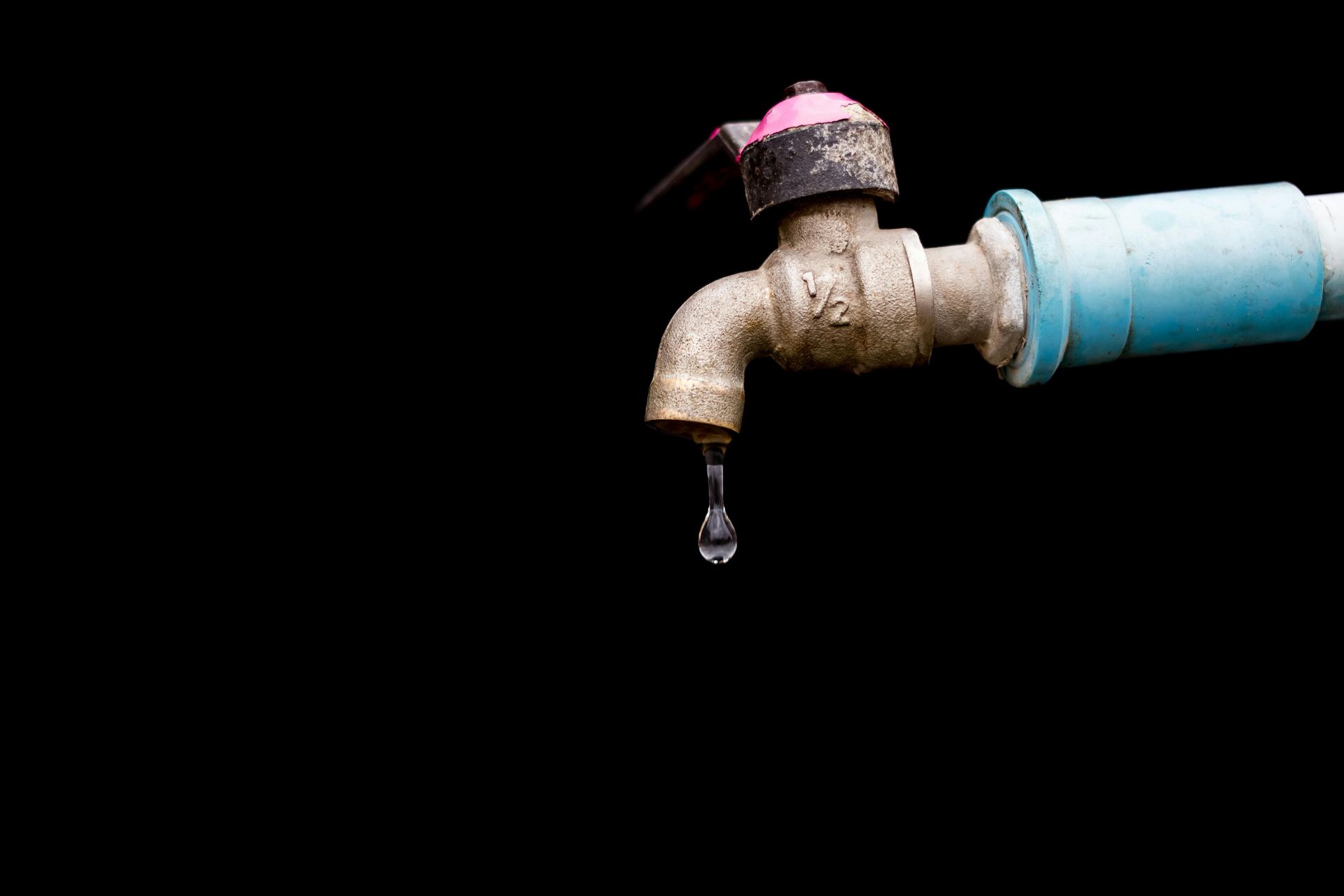 A rusty faucet dripping water with a black background.