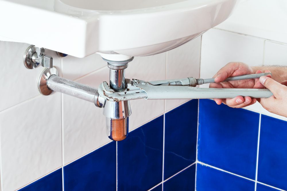 A Person Tightening a Chrome Sink Pipe Under a White Bathroom Sink — New Gen Plumbing and Gas in Kingscliff, NSW