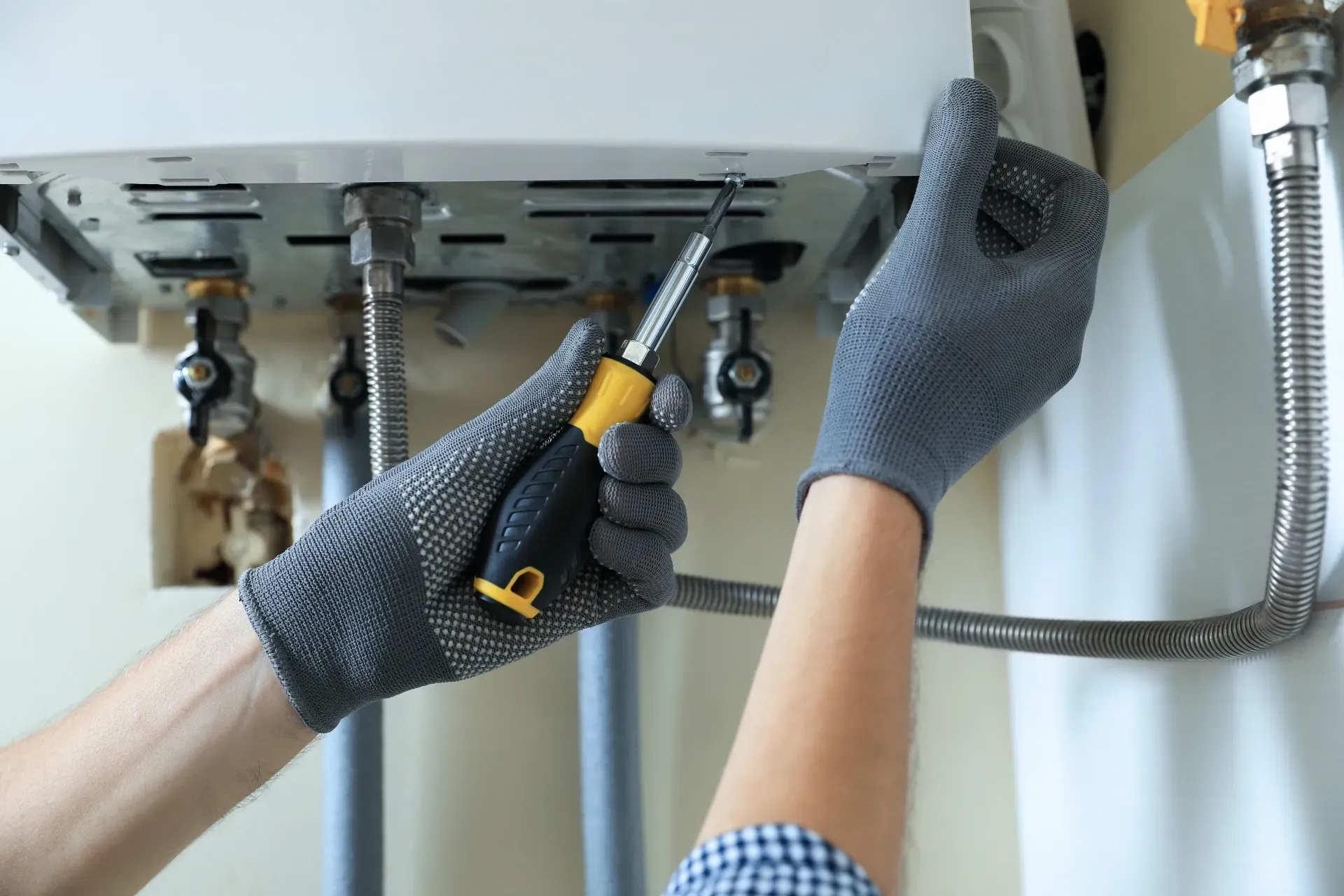 Gloved hands tightening plumbing fittings under a sink with a wrench — New Gen Plumbing and Gas in Banora Point, NSW