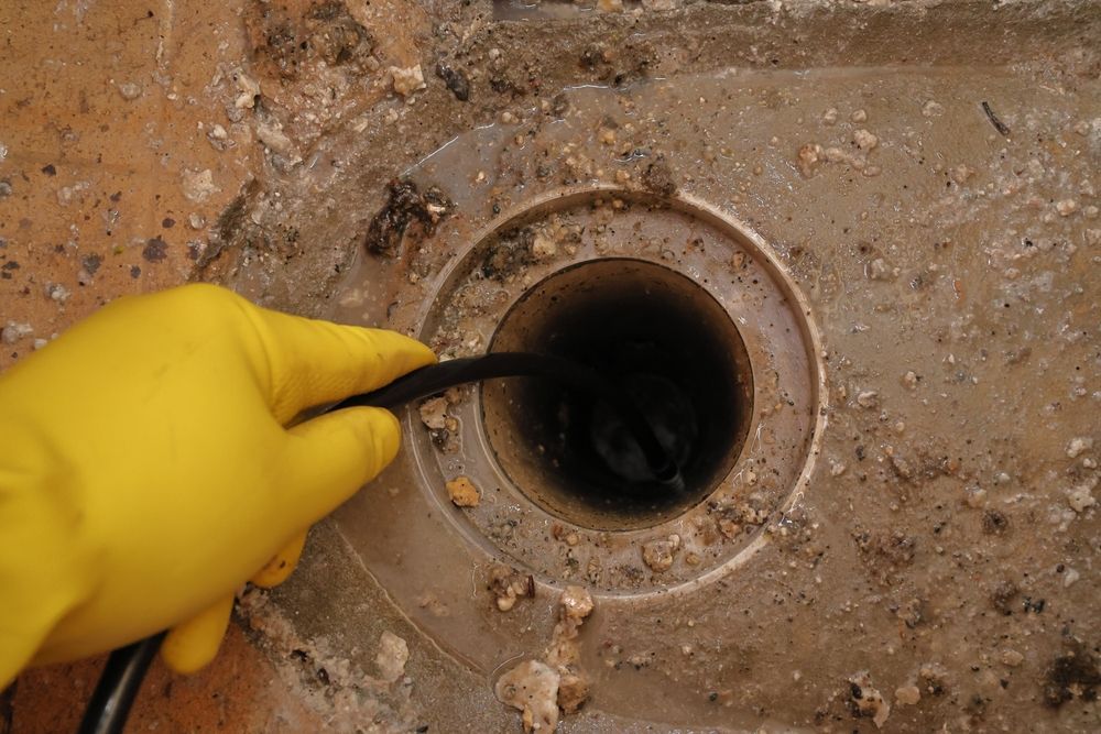 Yellow-gloved Hand Using a Black Cable to Inspect a Round Drain — New Gen Plumbing and Gas in Banora Point, NSW