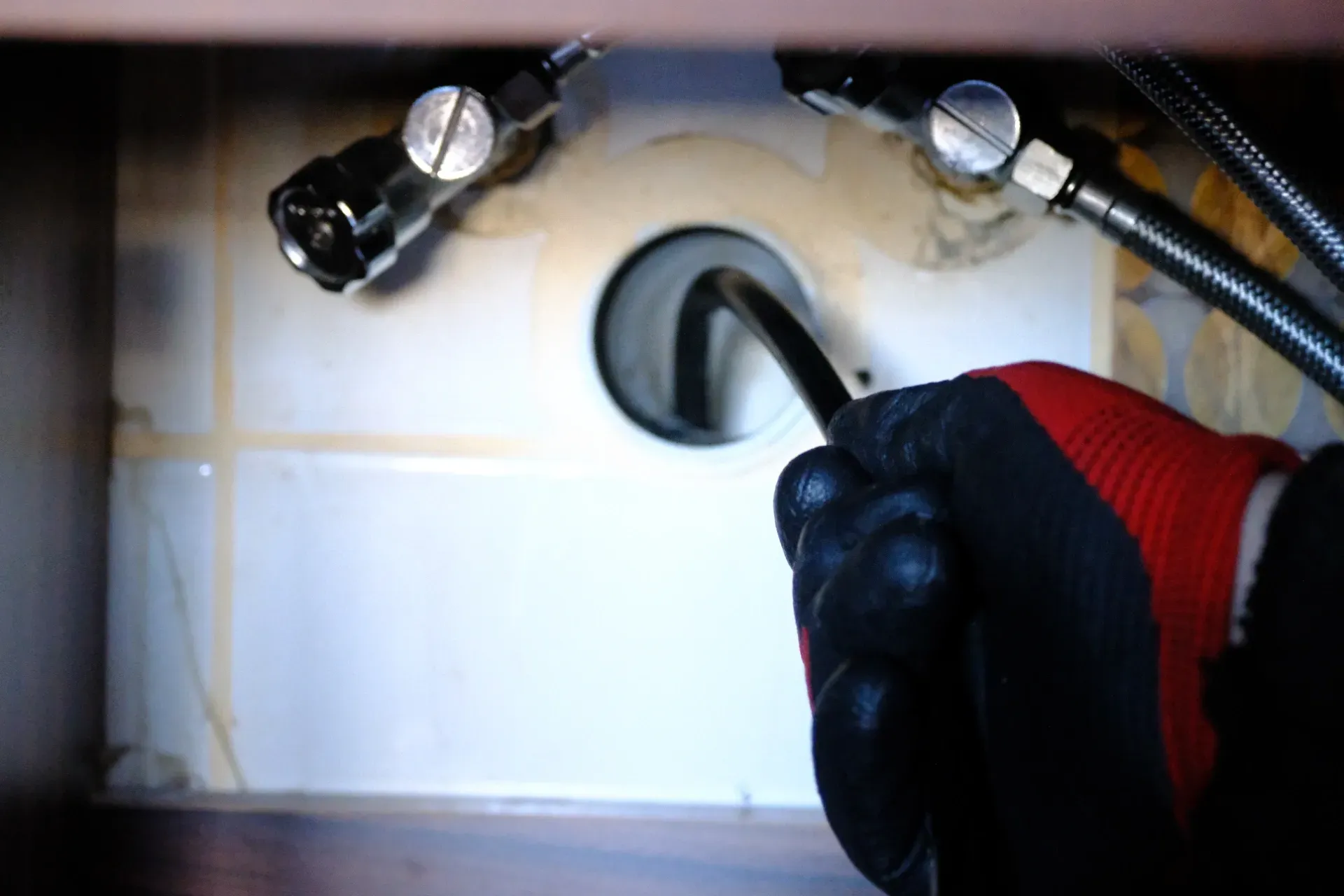 Gloved hands holding two metal hose connectors near a wall-mounted pipe opening — New Gen Plumbing and Gas in Banora Point, NSW