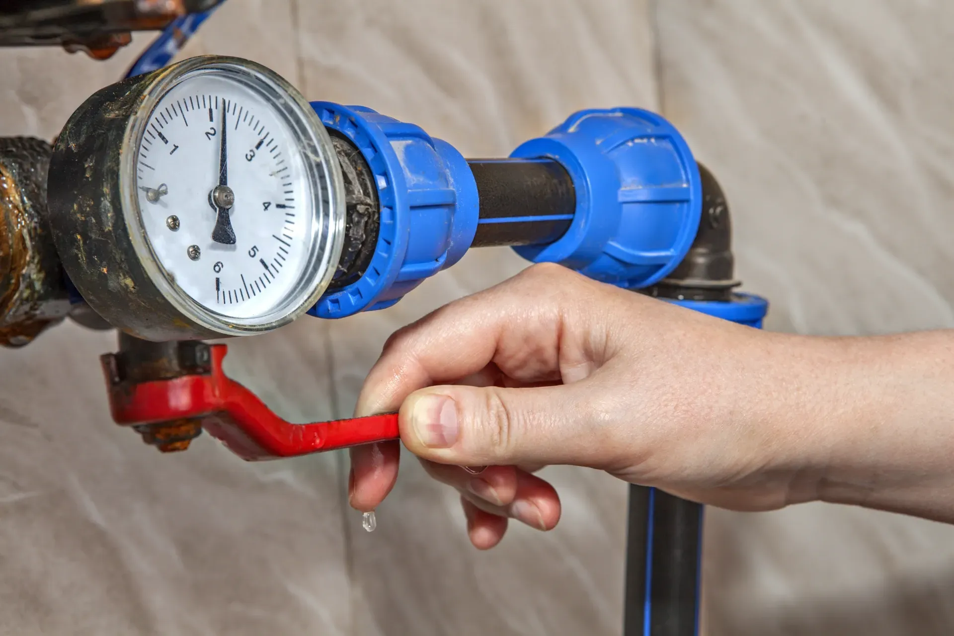 Hand turning a red valve beside a blue water meter with a gauge — New Gen Plumbing and Gas in Banora