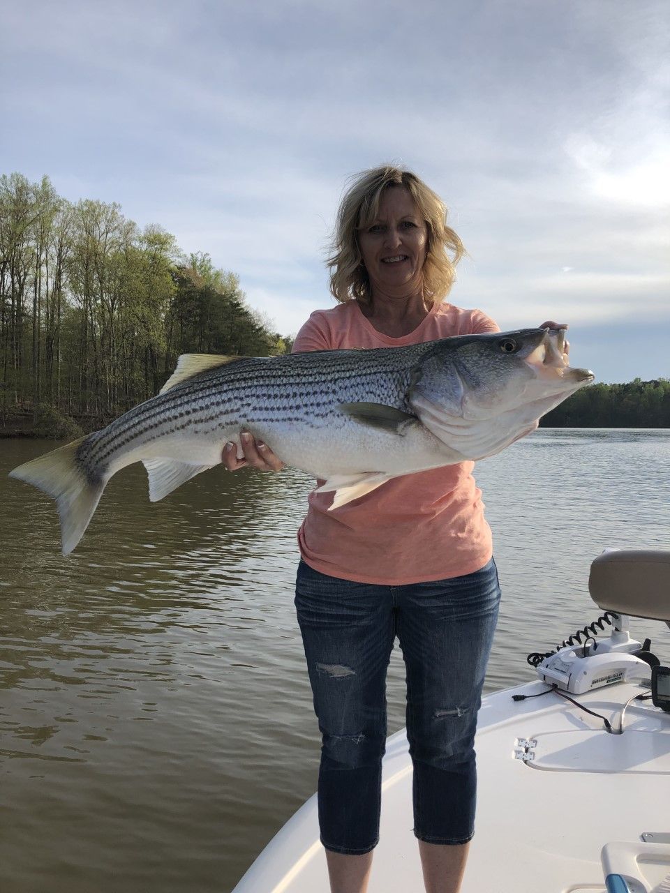 Woman on a boat holding a large striped fish by the water