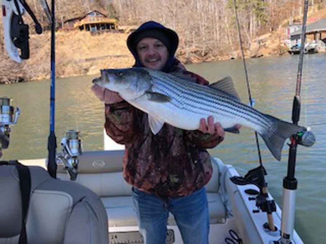 Person on a boat holding a large striped fish on a lake outdoors