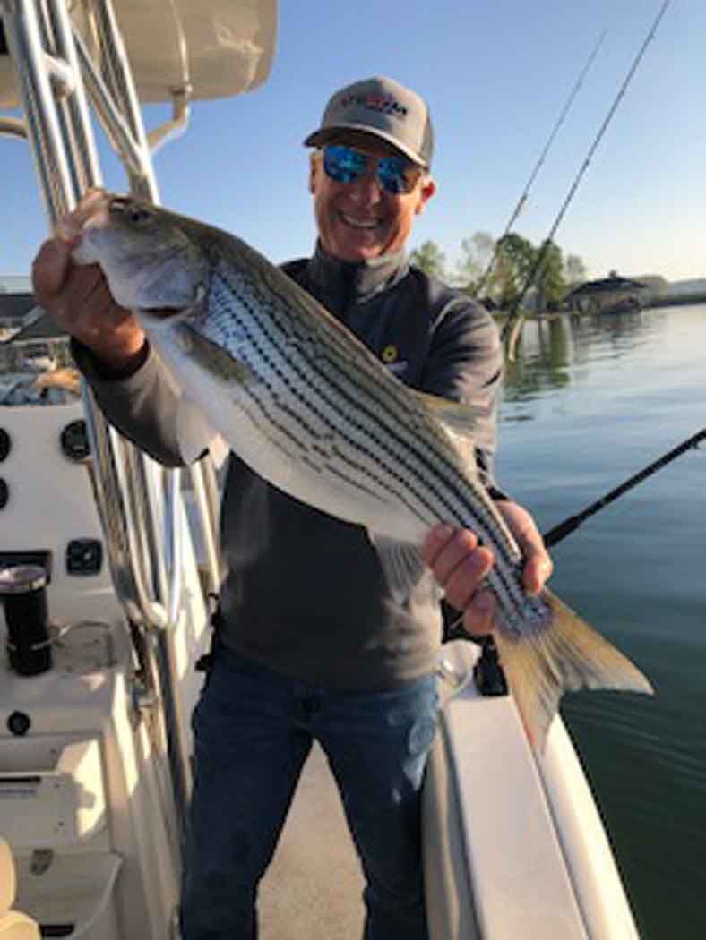 Man on a boat holding a large striped fish at sunrise on calm water