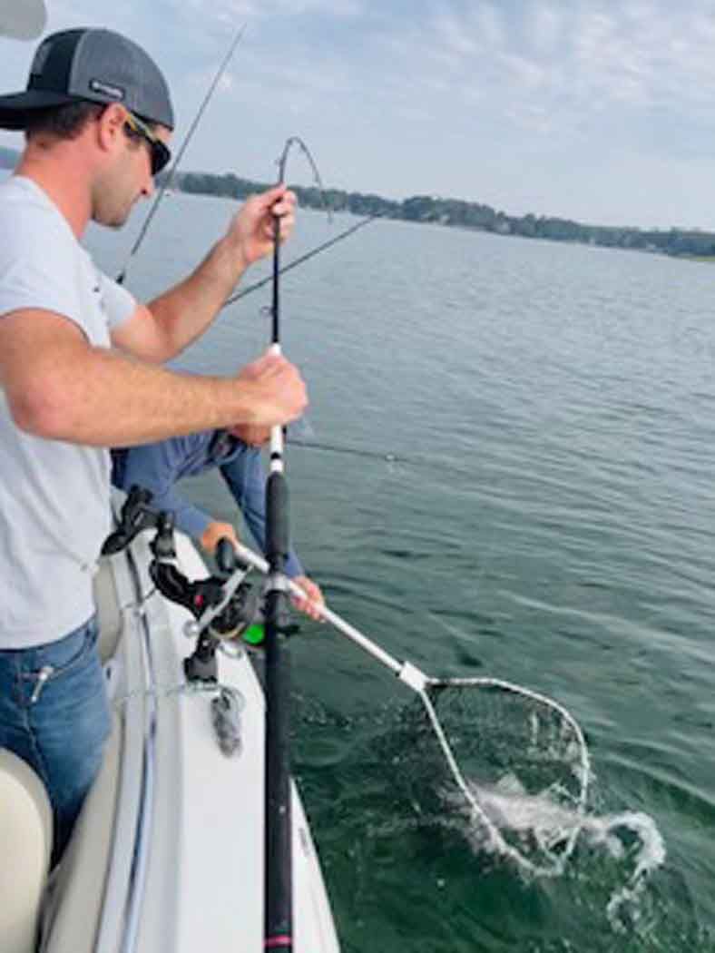 Person fishing from a boat, reeling in a fish on a calm lake.