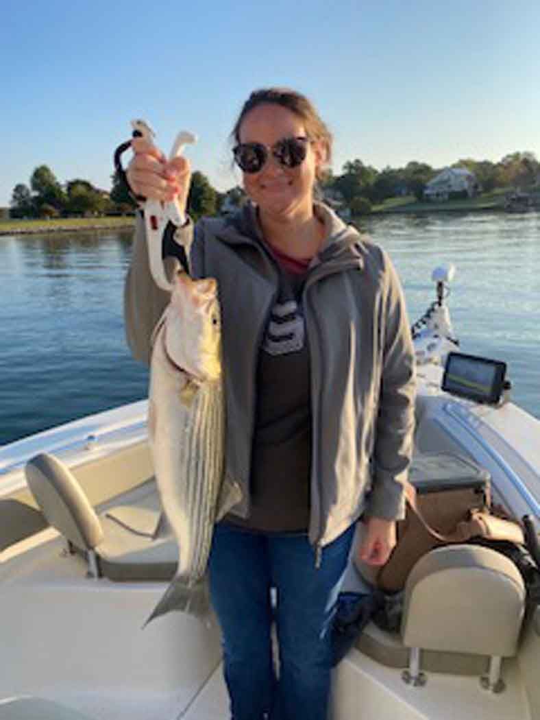 Person on a boat holding up a large striped fish on a calm lake at sunset