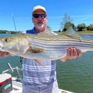 Man holding a large striped fish on a boat with calm water and blue sky behind him