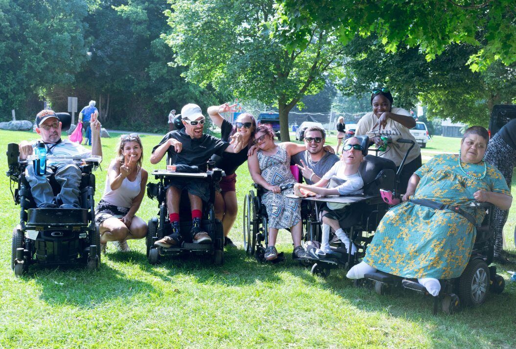 A group of people in wheelchairs are posing for a picture in a park.