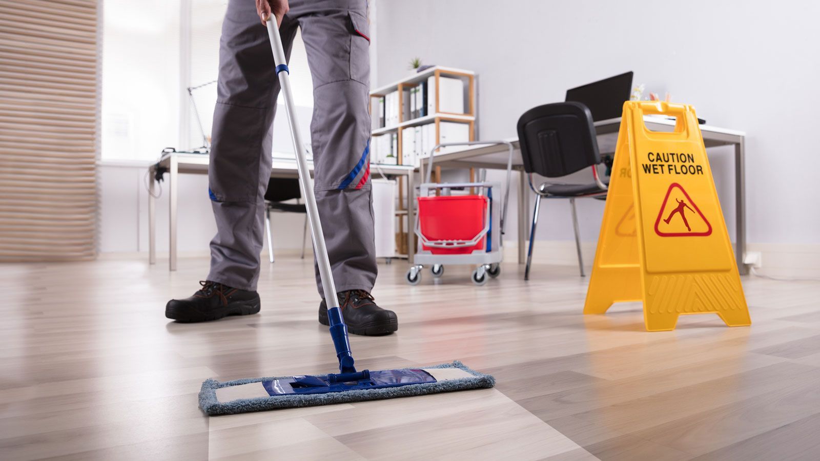 A man is mopping the floor in an office next to a caution sign.