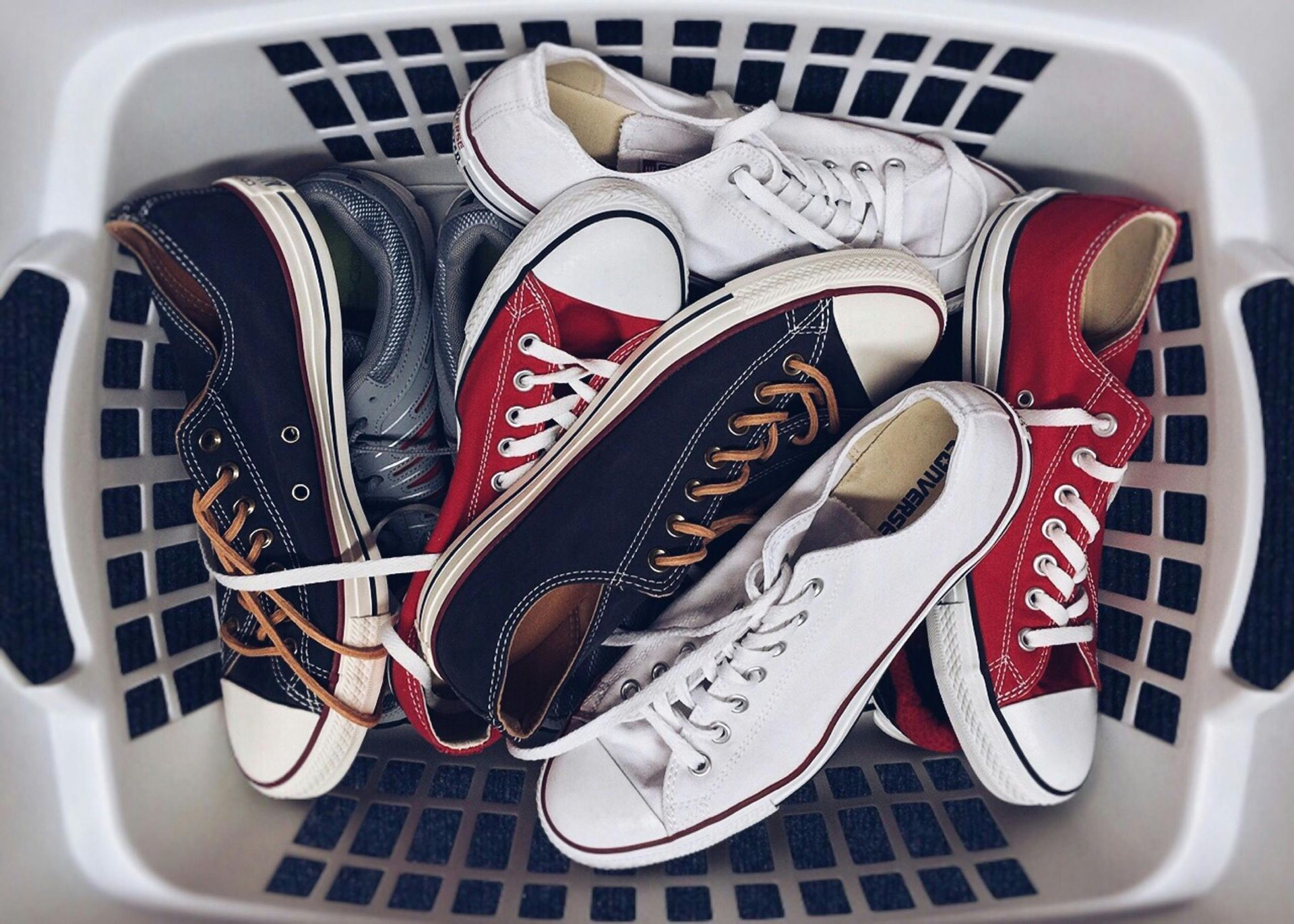 A laundry basket filled with a variety of shoes including converse