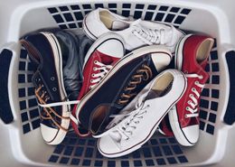 A laundry basket filled with a variety of shoes including converse