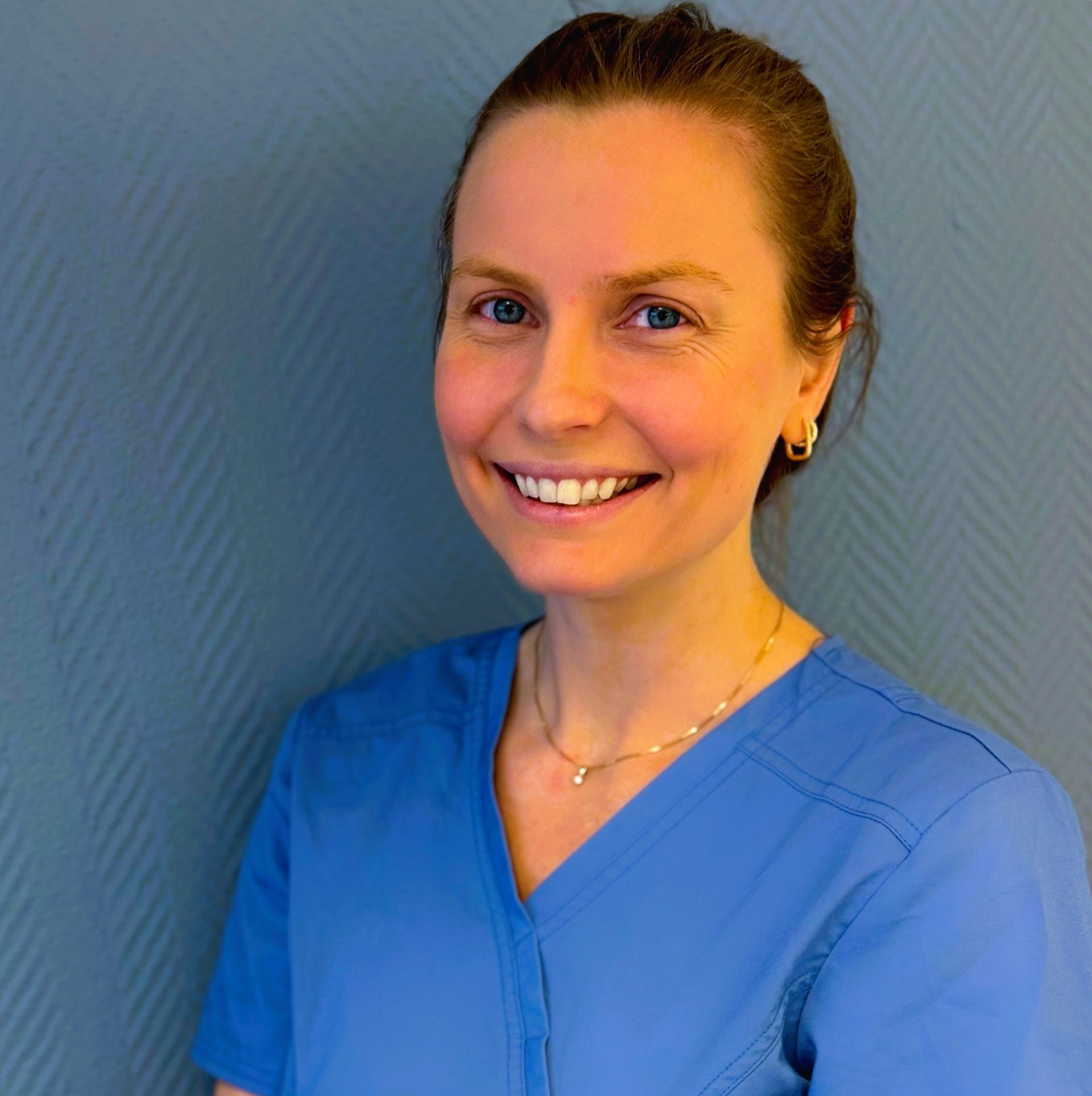 Tannlege Christian med briller og skjegg, iført blå skjorte og medisinsk maske, smiler til kameraet.