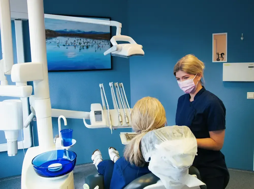 Seks kvinner i skrubber smiler i lyse omgivelser innendørs.