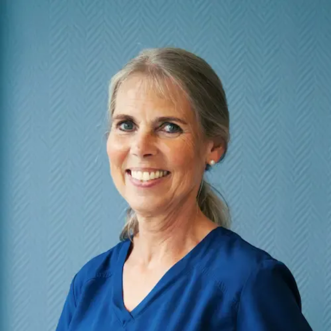 Tannlege Christian med briller og skjegg, iført blå skjorte og medisinsk maske, smiler til kameraet.