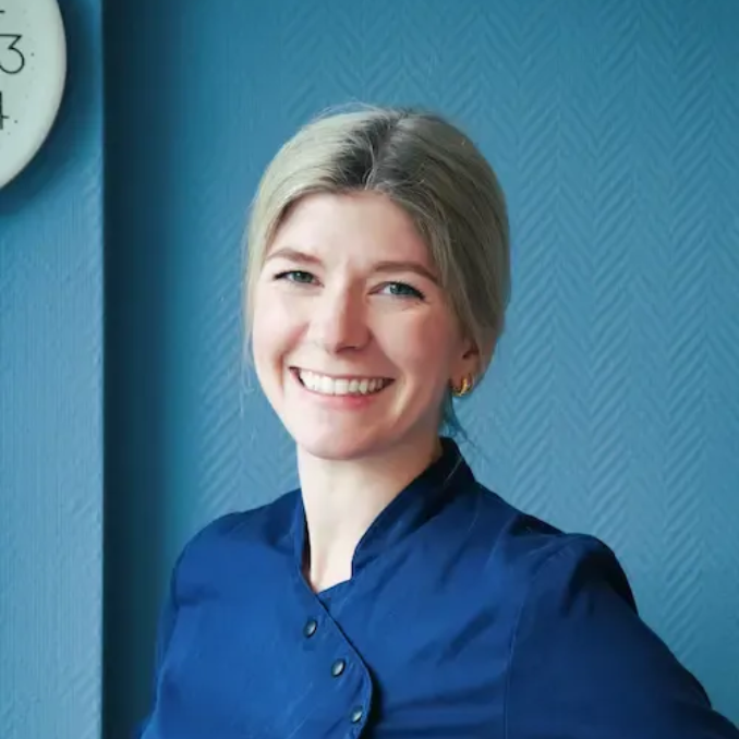 Tannlege Christian med briller og skjegg, iført blå skjorte og medisinsk maske, smiler til kameraet.