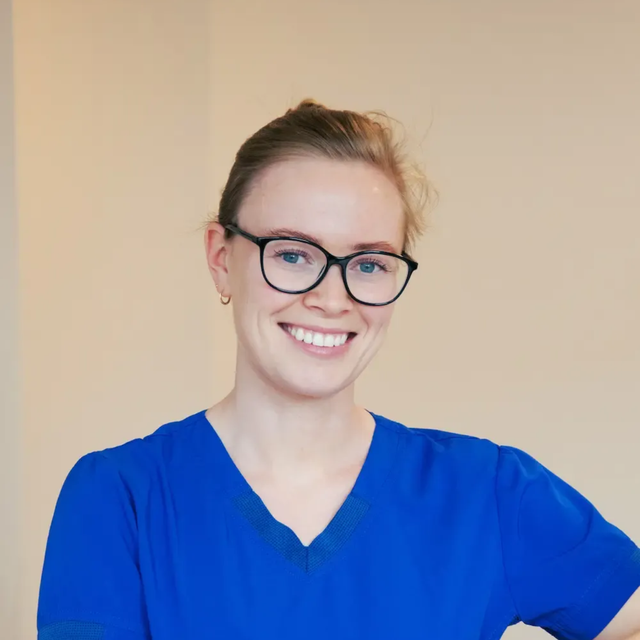 Tannlege Christian med briller og skjegg, iført blå skjorte og medisinsk maske, smiler til kameraet.