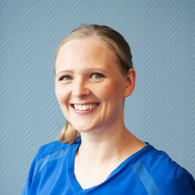 Tannlege Christian med briller og skjegg, iført blå skjorte og medisinsk maske, smiler til kameraet.