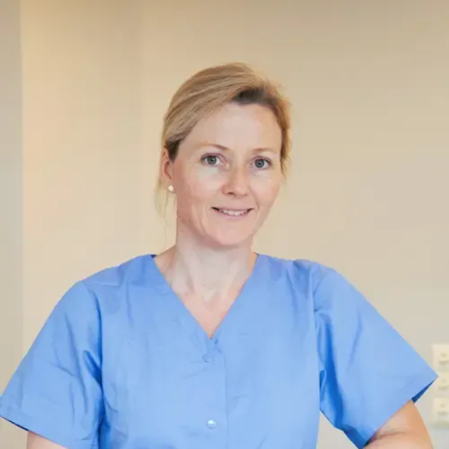 Tannlege Christian med briller og skjegg, iført blå skjorte og medisinsk maske, smiler til kameraet.