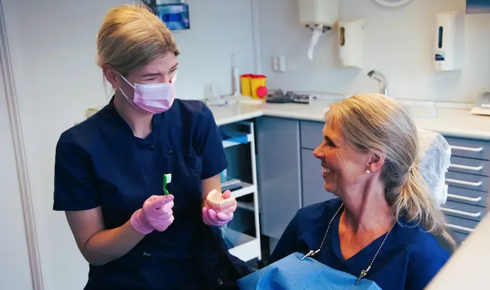 Kvinne som smiler, med vind i håret, utendørs, iført rosa jakke, naturskjønn bakgrunn.