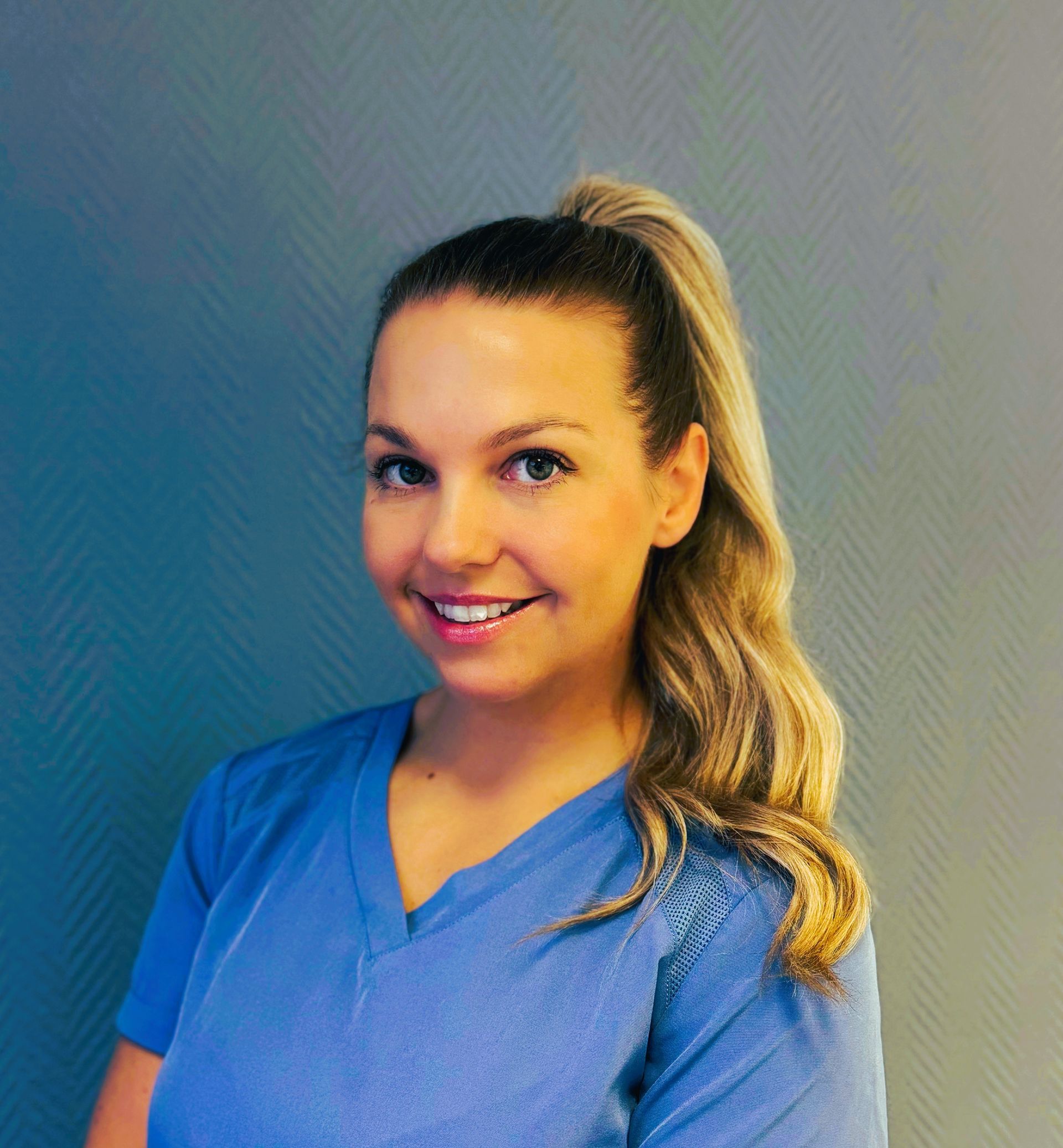 Tannlege Christian med briller og skjegg, iført blå skjorte og medisinsk maske, smiler til kameraet.