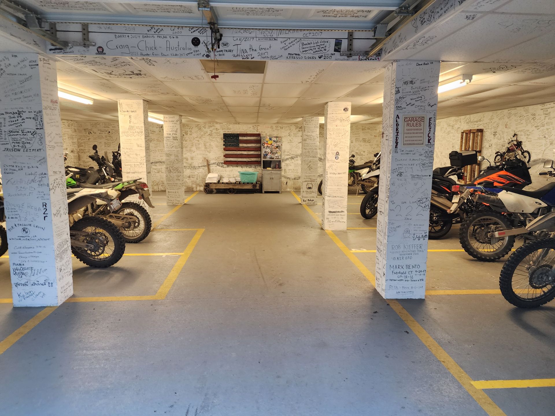 Parking garage with motorcycles parked in designated spots, American flag on the back wall.