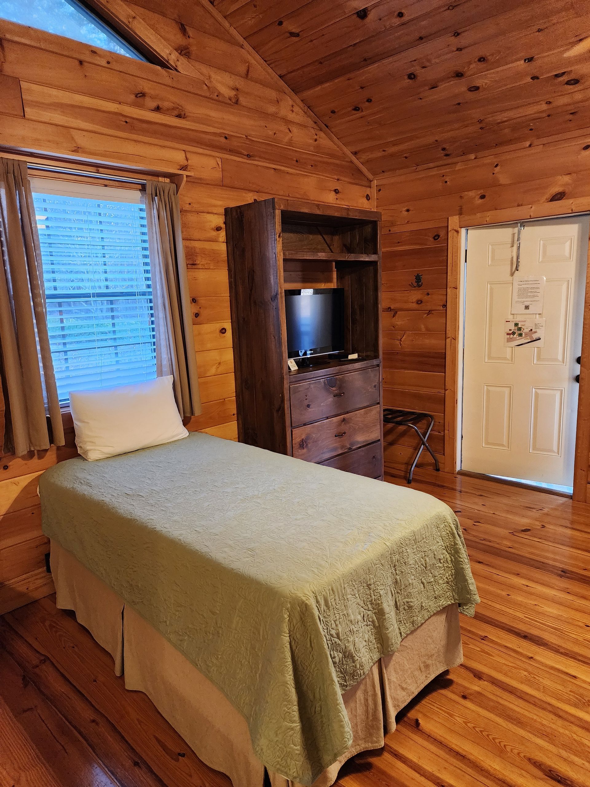 Bedroom with wooden walls, a single bed, a wooden cabinet, and a door.
